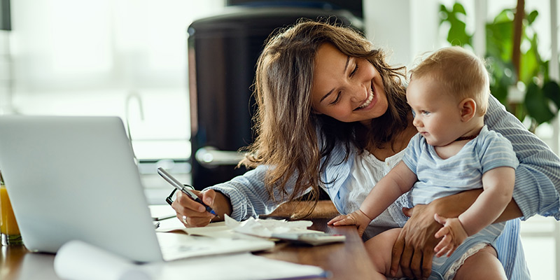Mother smiling with baby on her lap, looking at her financials.